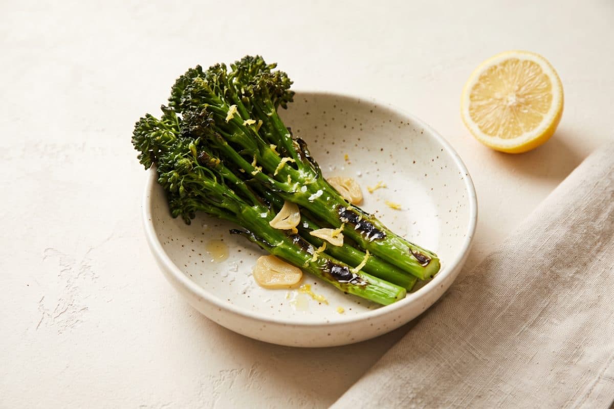 Charred Lemon Broccolini, finished with lemon, served as one portion in a speckled cream bowl