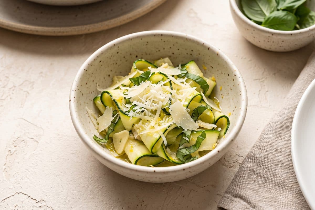 Parmesan Zucchini Ribbons, finished with grated Parmesan and lemon zest, served as one portion in a speckled cream bowl