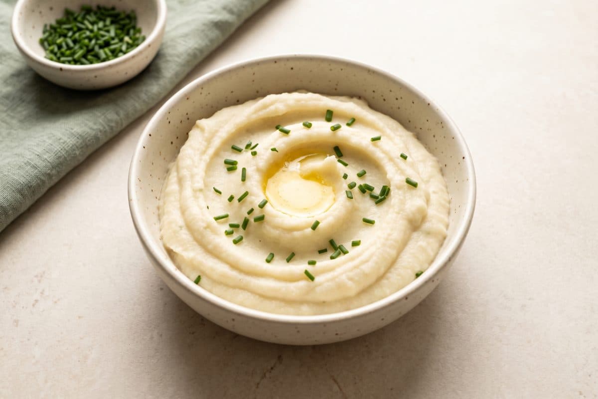 Roasted Garlic Cauliflower Mash, finished with chives, served as one portion in a speckled cream bowl